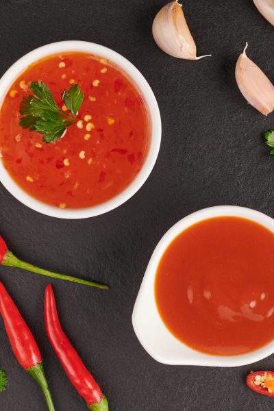 red hot chilli sauce. tomato ketchup, chilli sauce, puree with chili pepper, Vegetables, tomatoes and garlic. on on black stone background. top view